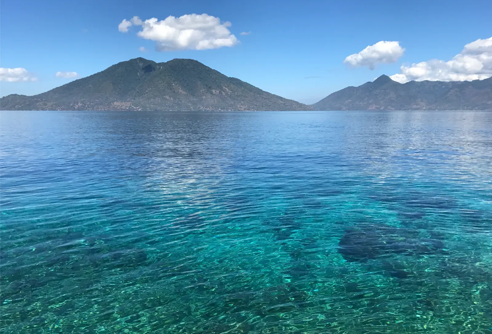Crystal-clear turquoise water off Pura Island with a volcanic peak rising across the strait