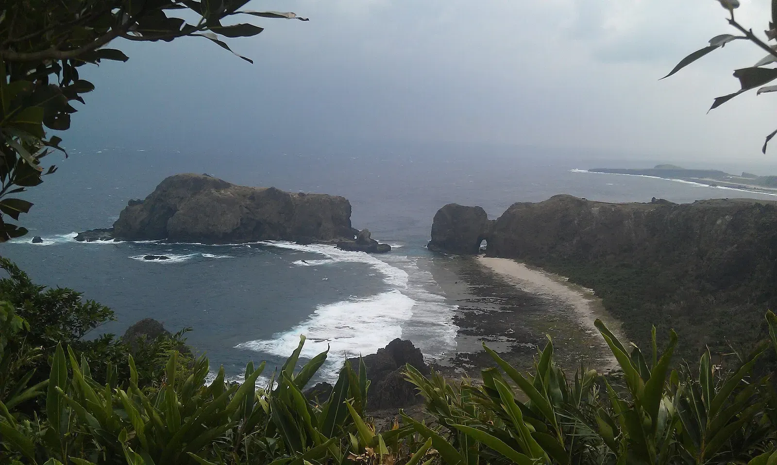 Rocky headland and sandy cove with breaking waves on Green Island's coastline