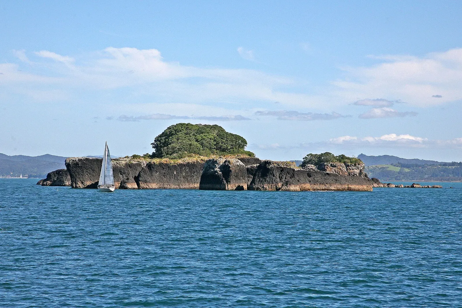 A small basalt island rises from blue water in the Bay of Islands