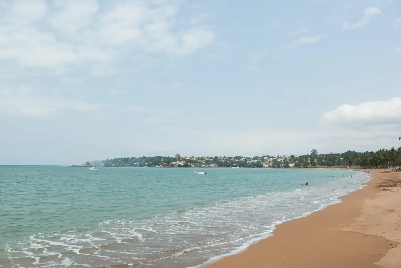 A turquoise bay lined with sand and palm trees curves toward a small coastal town on São Tomé island