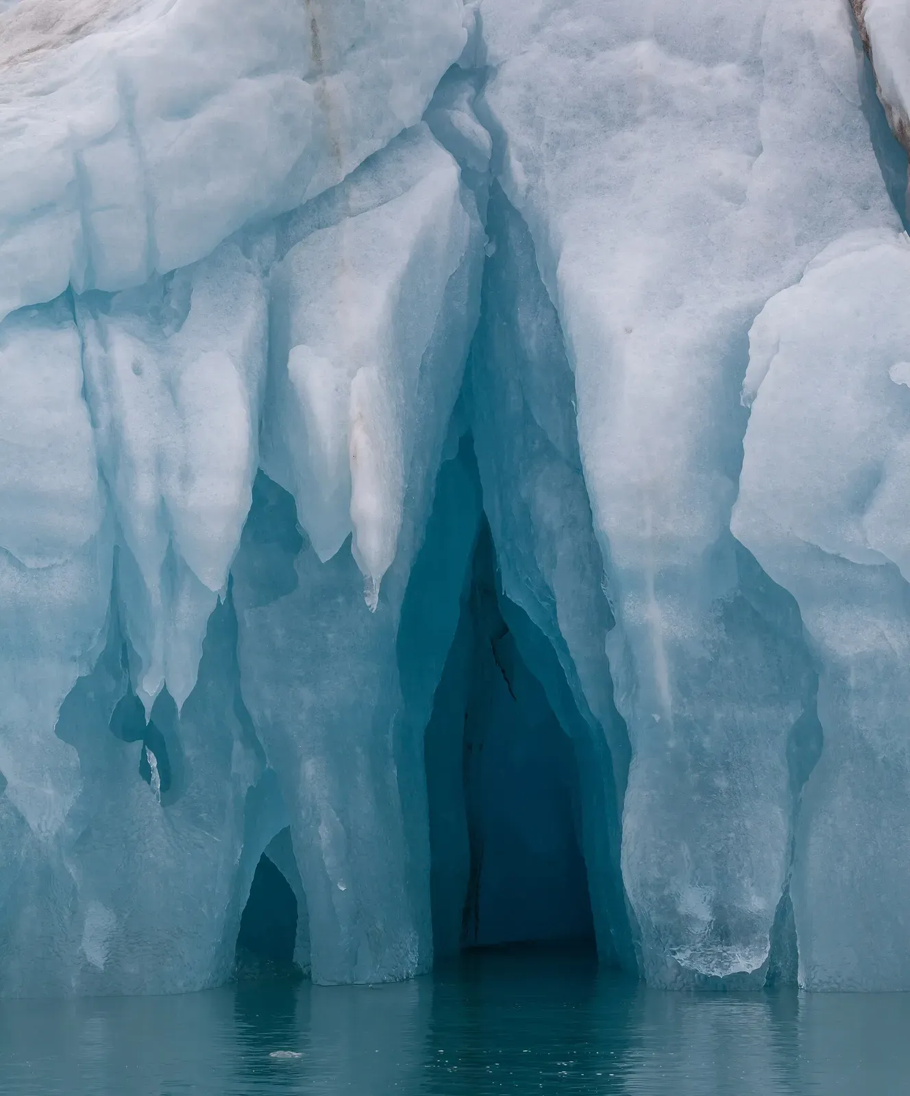 A carved blue ice cave opening at the waterline of an iceberg in Liefdefjord