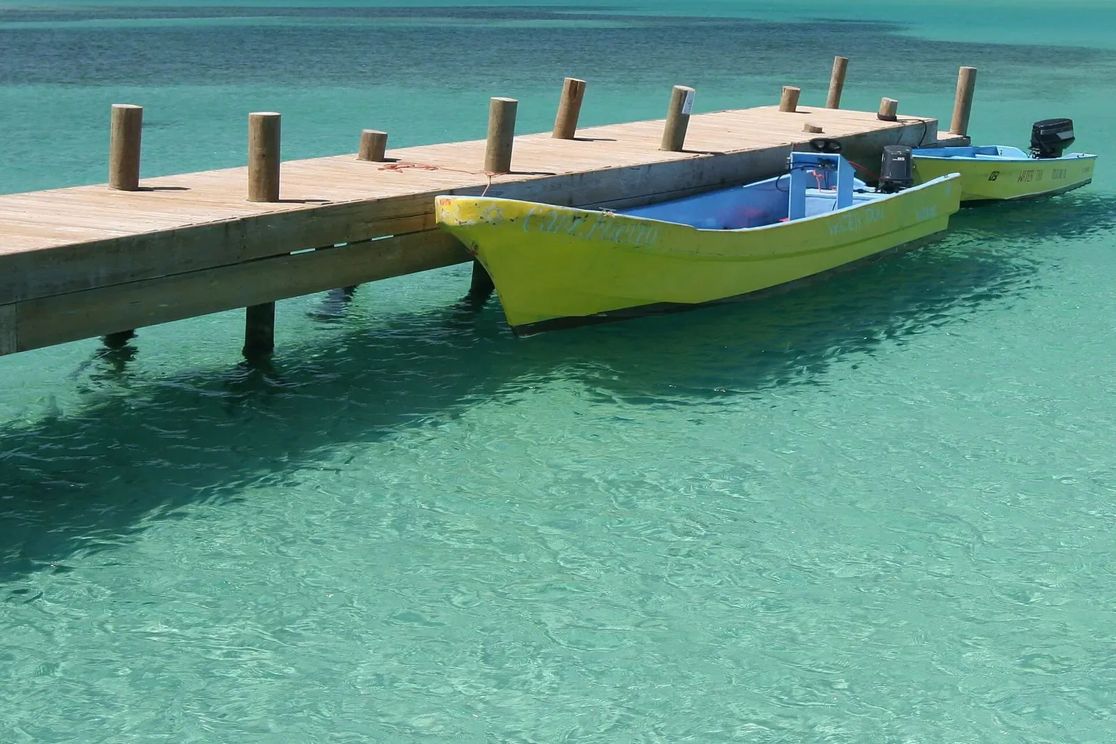 Small tender boats moored at a wooden dock in clear turquoise bay water off Roatán.