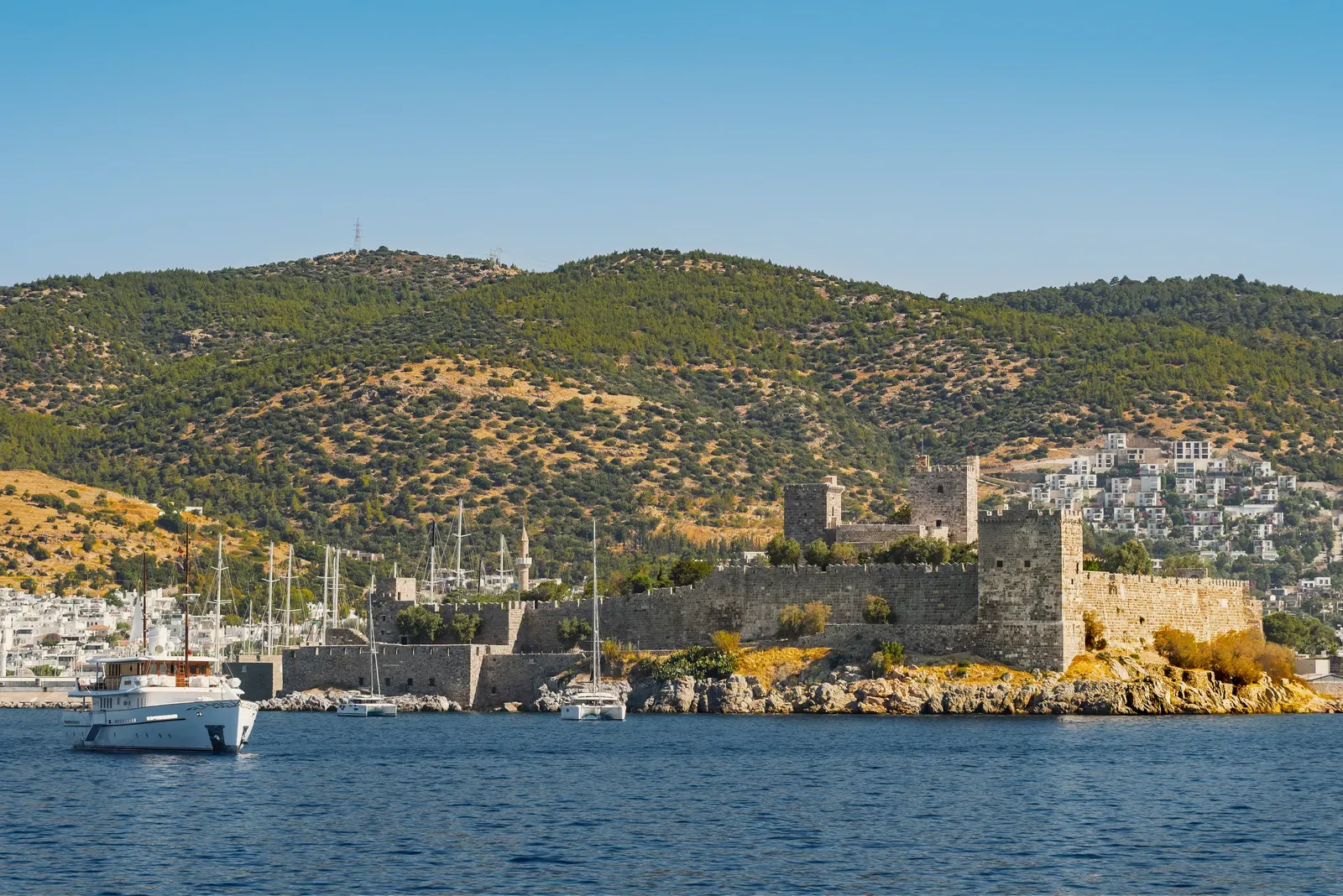 Rocky shore of Bodrum Castle seen from the water with boats at anchor
