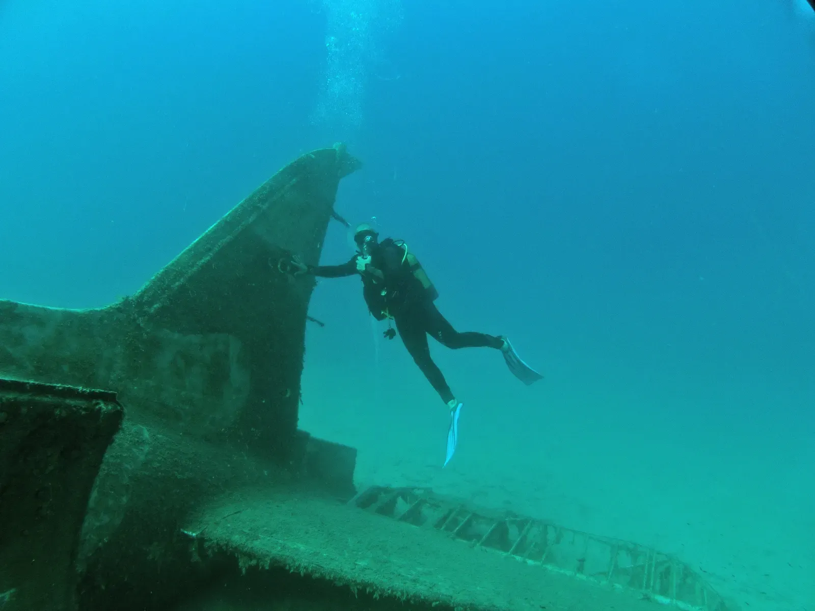 Diver beside the tail fin of the C-47 Dakota wreck on the sandy seabed off Kaş