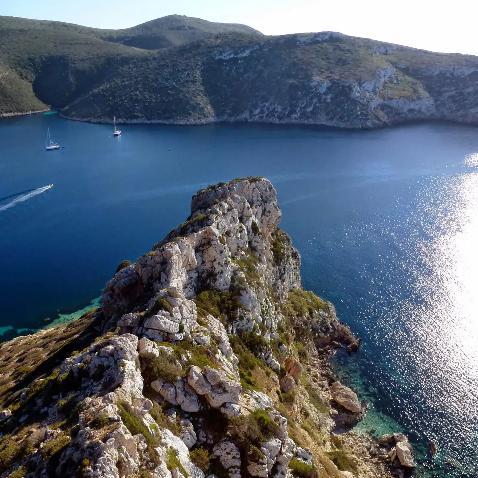 Limestone ridge dropping into clear blue water with sailboats anchored beyond