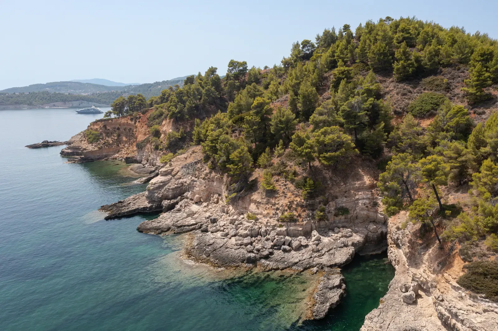 Pine-covered cliffs and clear rocky shallows on the Alonissos coastline