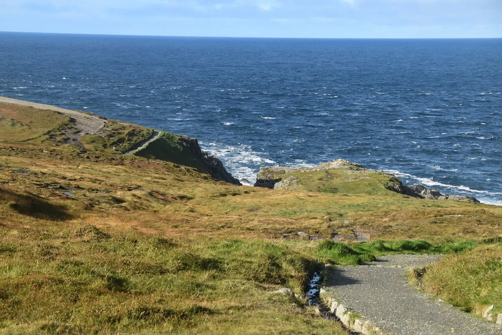 Grassy coastal path winding down rocky slopes to the blue Atlantic at Malin Head