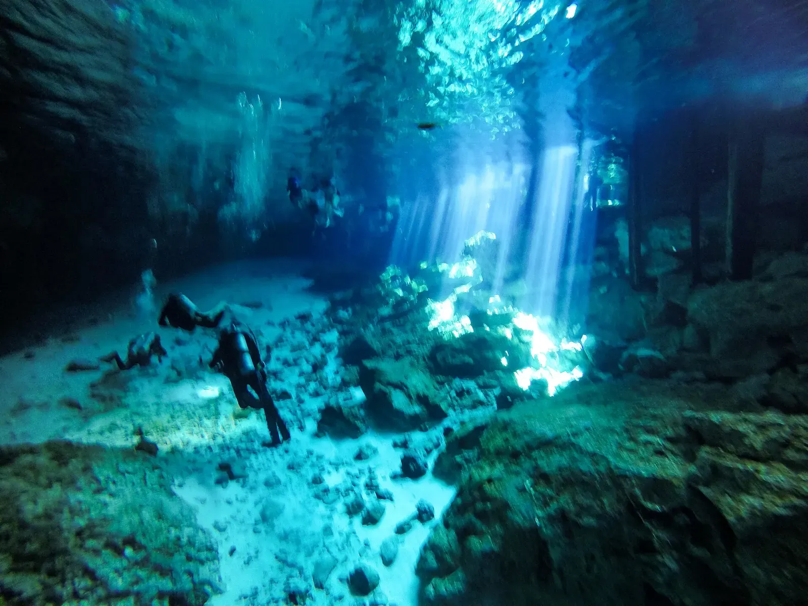 Cave diver descending through beams of sunlight inside a Yucatan cenote