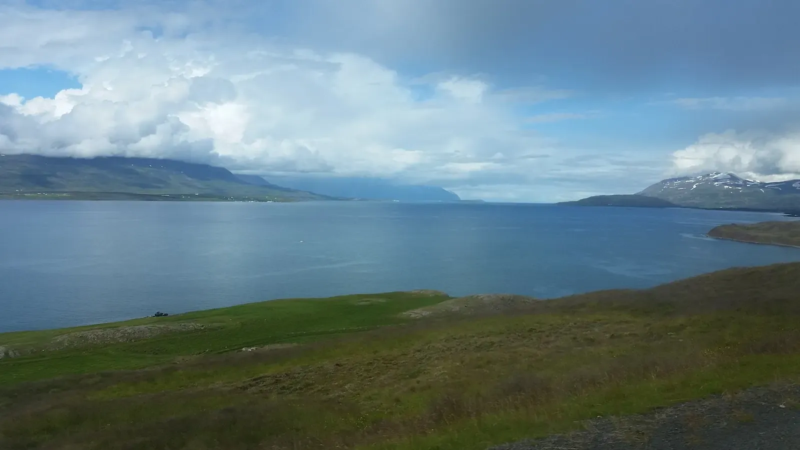 Sunlit peaks frame the wide blue waters of Eyjafjörður fjord under a partly clouded sky