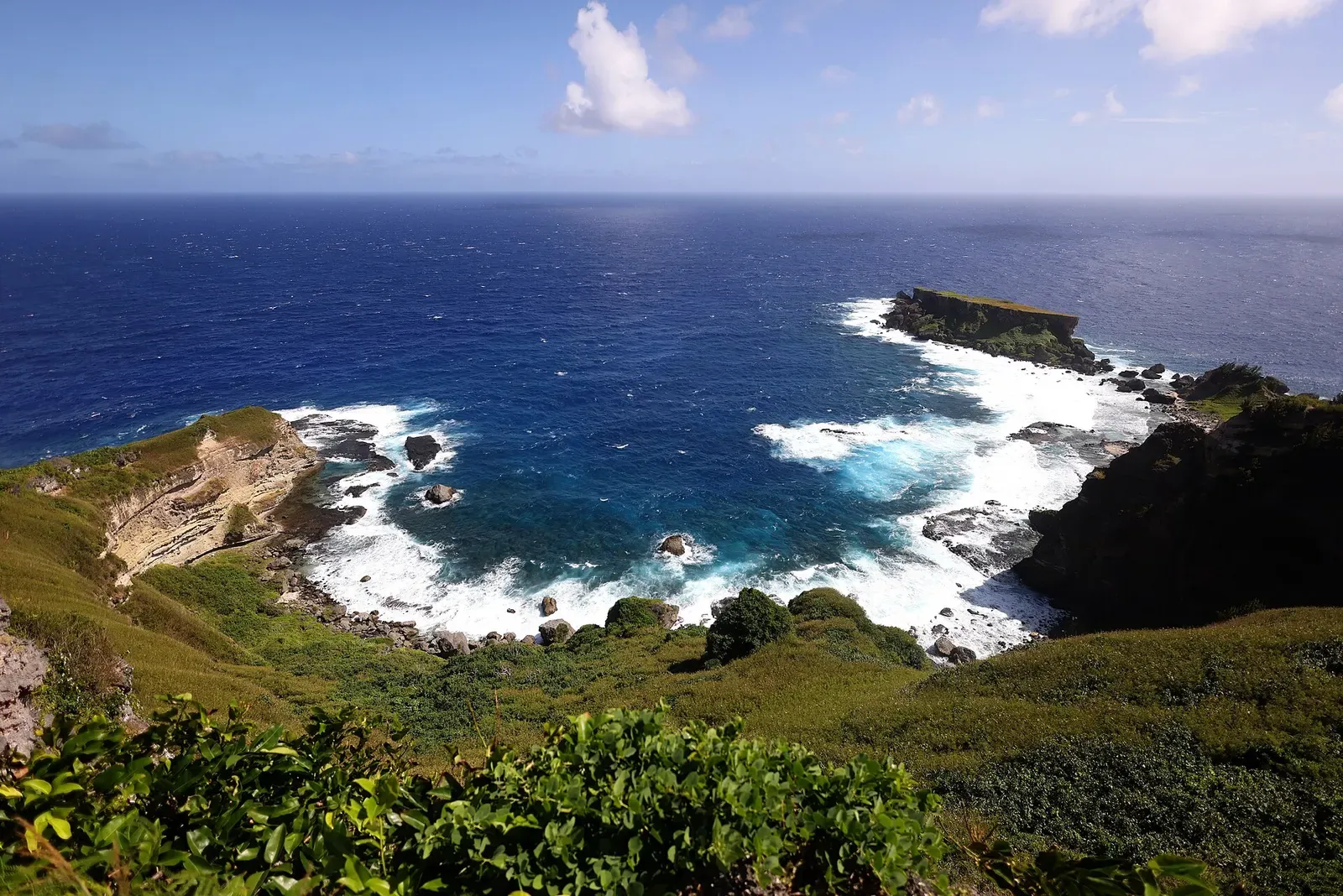 Dark blue Pacific swells breaking against jagged sea stacks off Saipan's rugged coastline