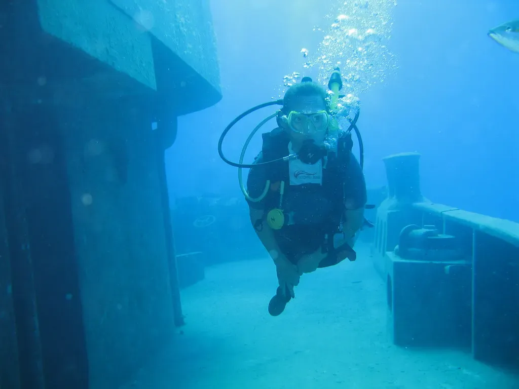 A diver hovers beside an open hatch on the hull of a sunken ship