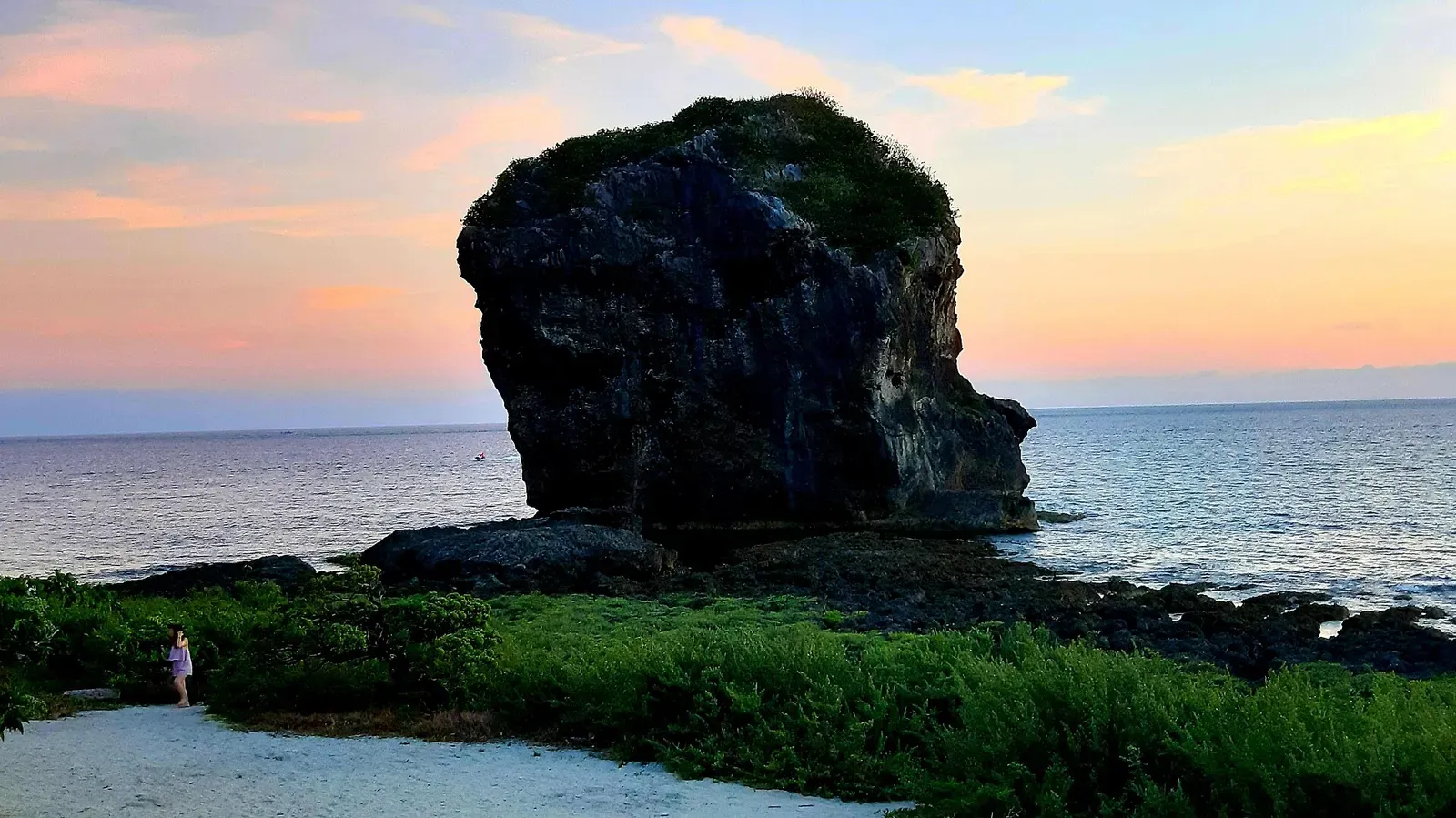 Chuanfan Rock, known as Sail Rock, silhouetted against a pink sunset sky on the Kenting coast.