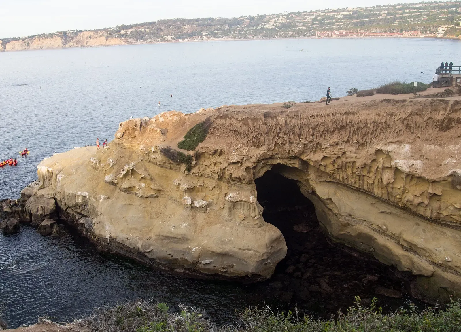 Sandstone cliff arch and sea caves at La Jolla Cove with visitors walking along the rim
