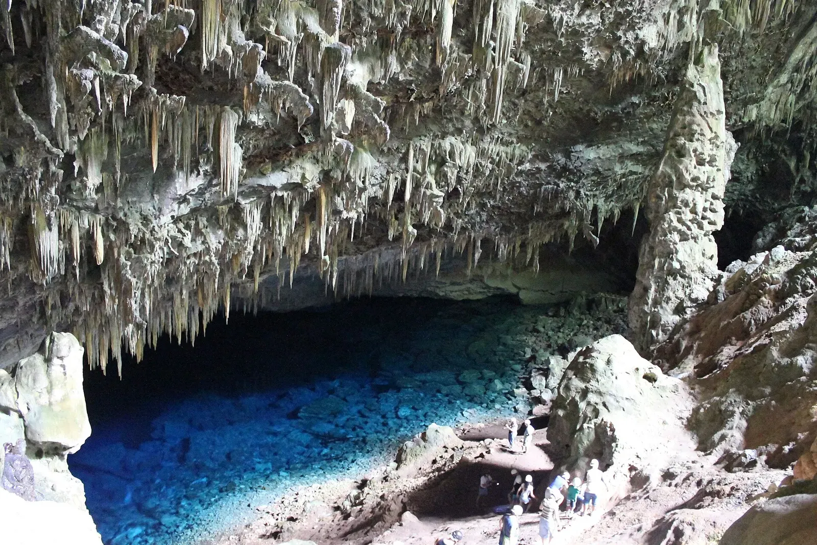 Visitors stand beside a deep blue karst lake inside a limestone cave near Bonito