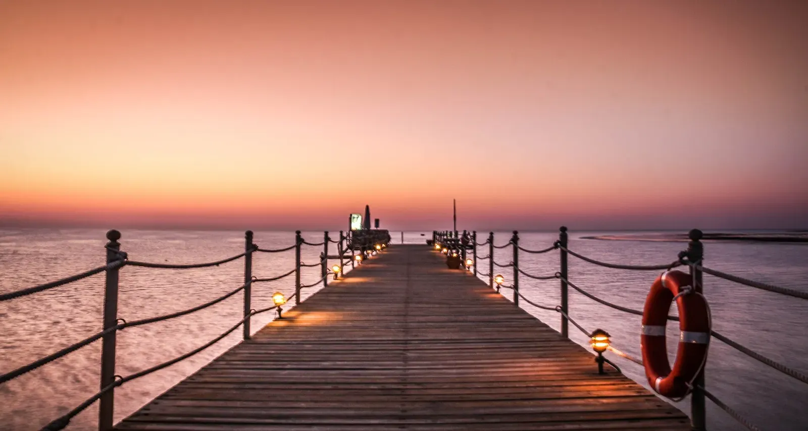 A wooden pier stretches into calm water under a pink sunrise sky at Marsa Alam