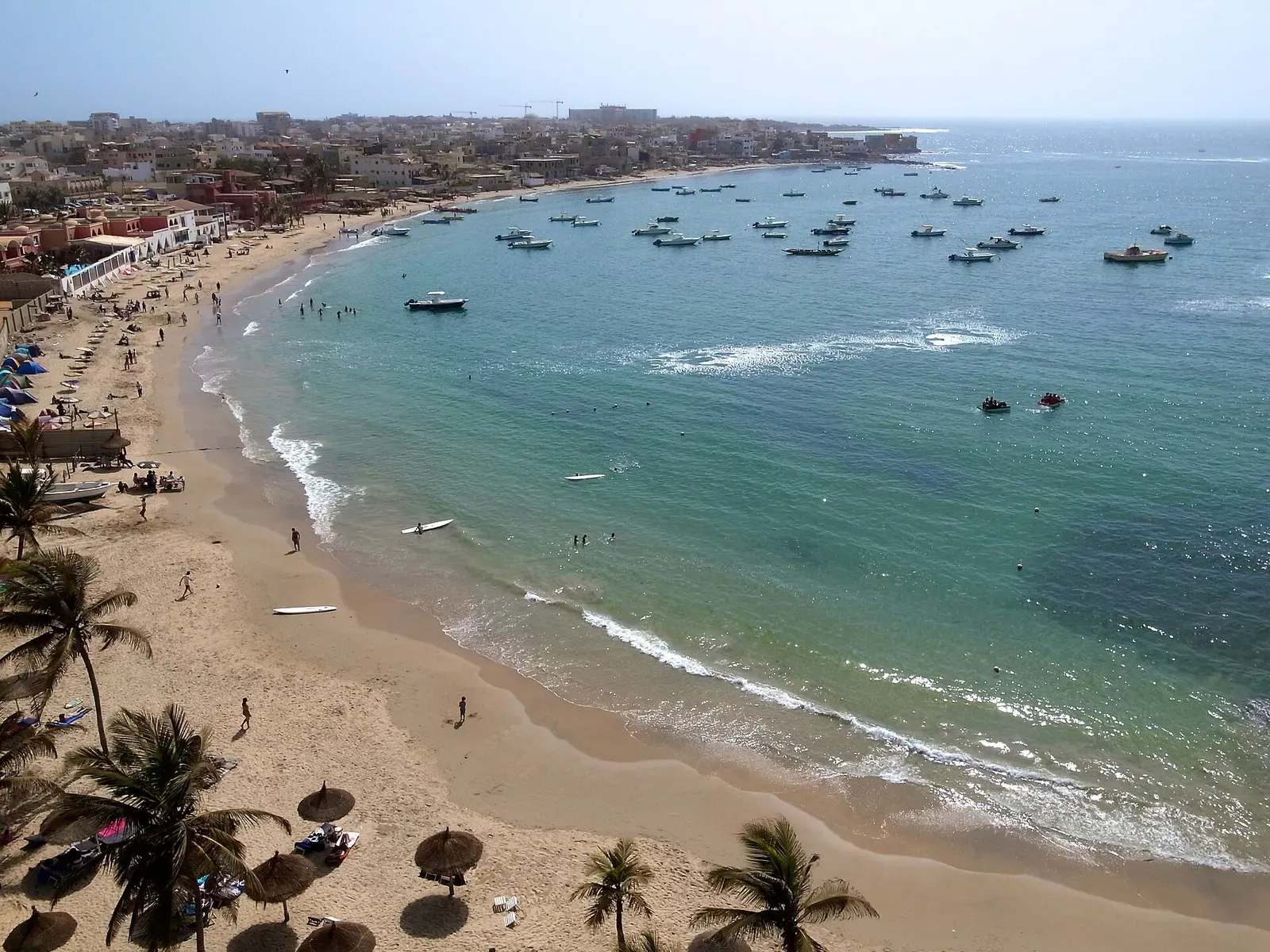 Small fishing boats anchored in Ngor Bay's turquoise water in front of the beach and village