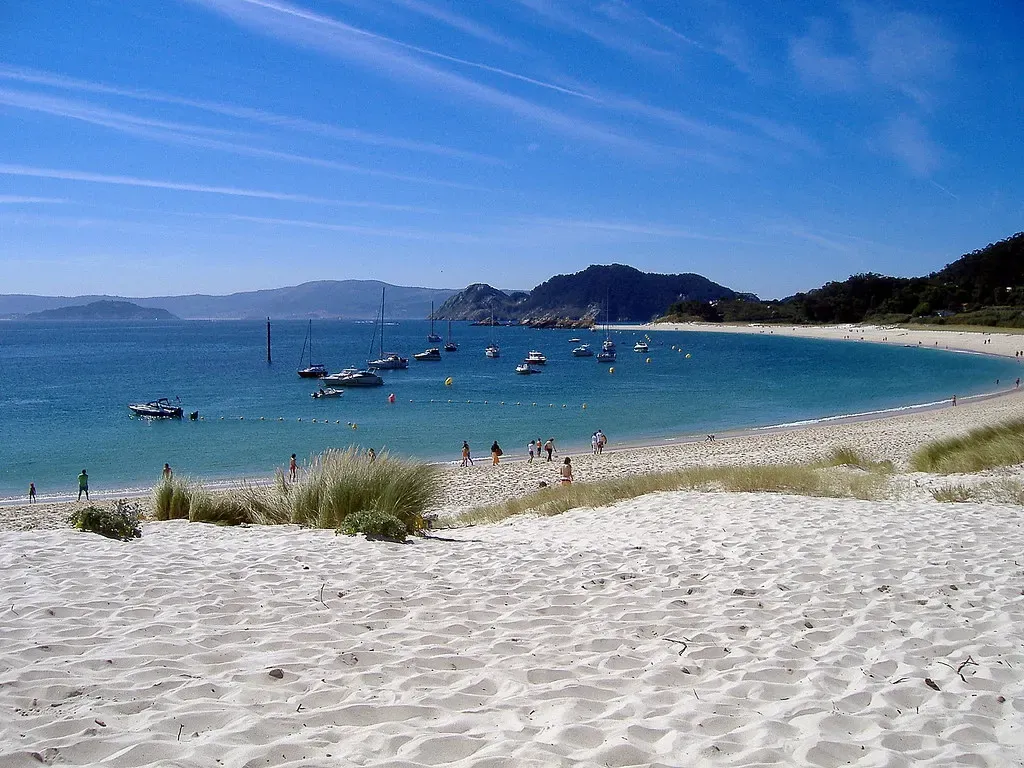 Praia de Rodas, the pale sandbar beach linking two of the Cíes islands, with small boats anchored in turquoise water.