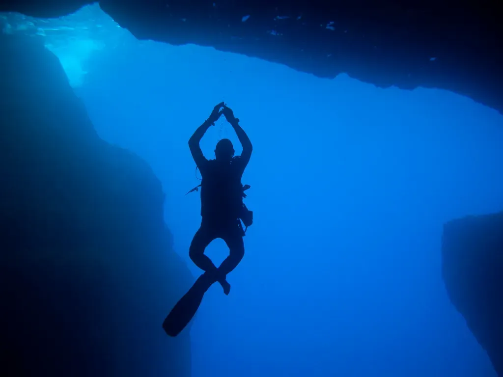 Diver silhouetted against blue light inside Cathedral Cave on Gozo