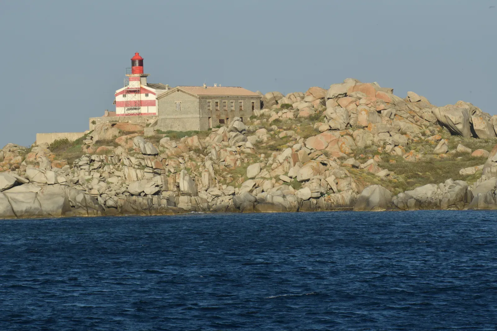 Red-and-white Lavezzi lighthouse on rounded granite boulders at the shoreline