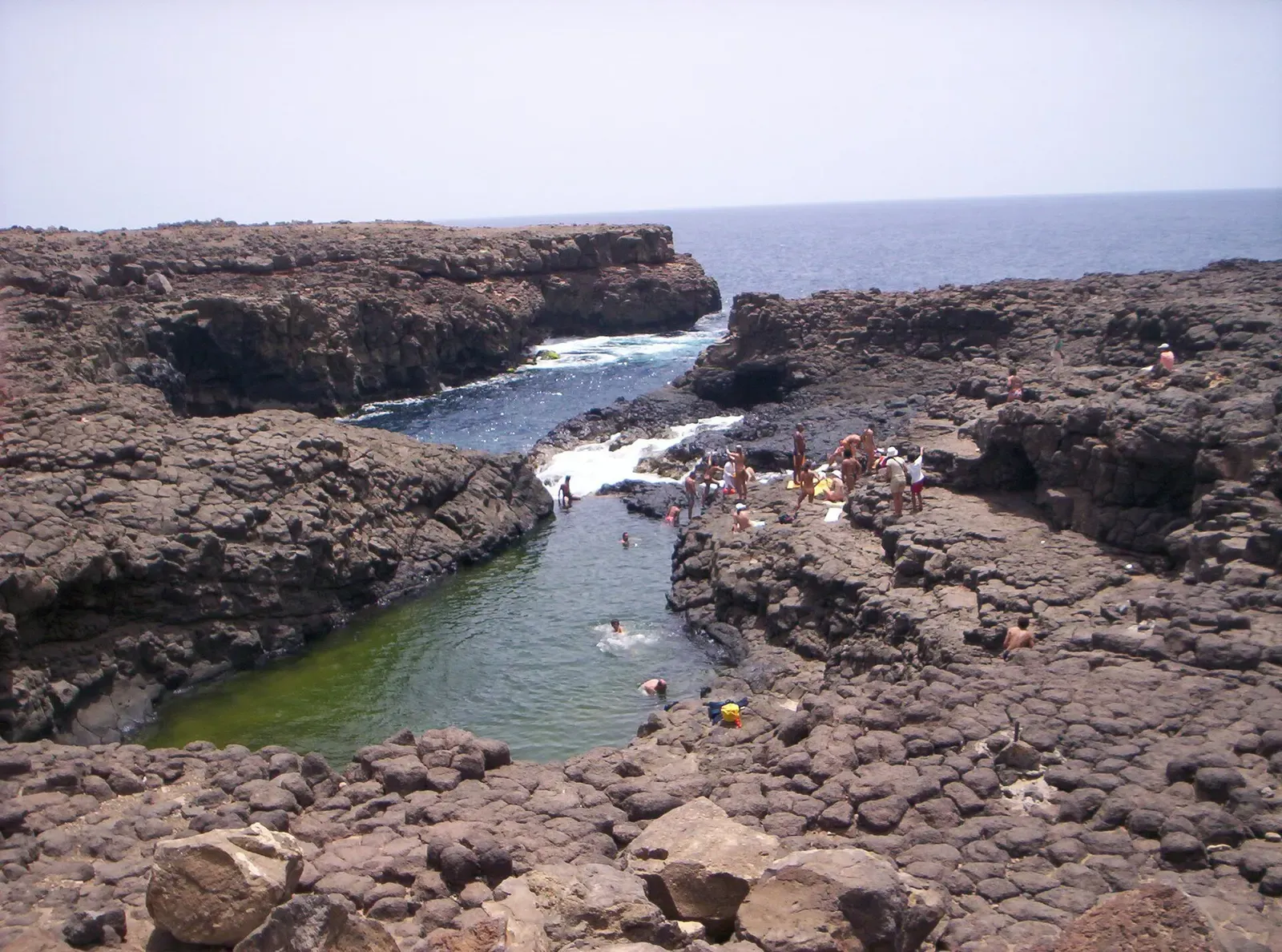 A natural pool cut into black volcanic rock connects to the ocean at Buracona on Sal island