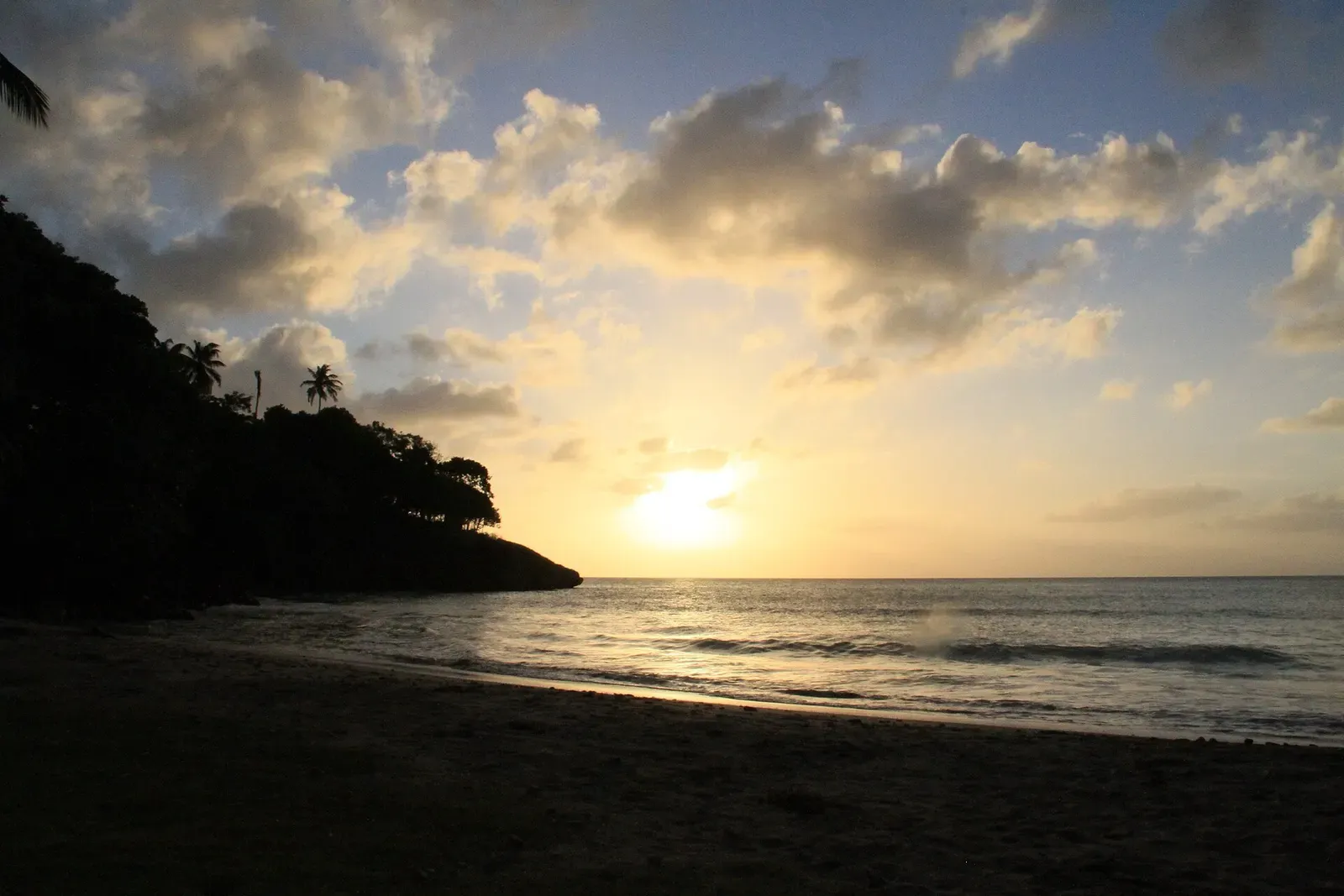 Silhouetted headland and palm trees against a sunset over calm water on Providencia's coast