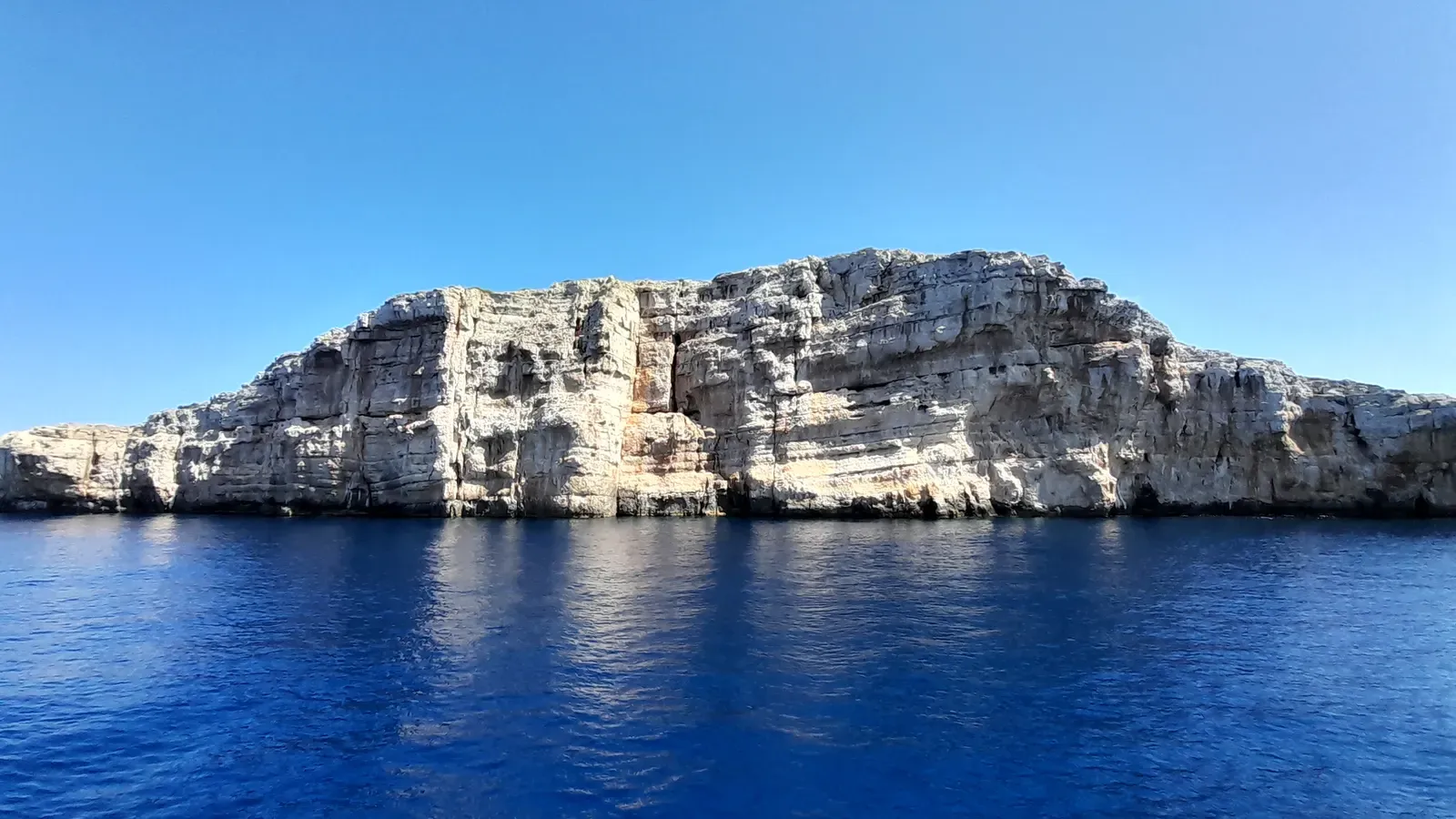 Sunlit limestone cliff face of Rašip Veli dropping into deep blue water in Kornati National Park
