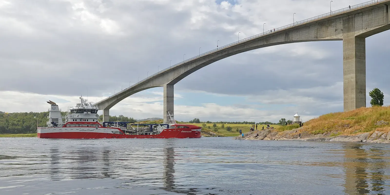 A cargo vessel passes beneath the arched Saltstraumen bridge as it threads the narrow tidal strait
