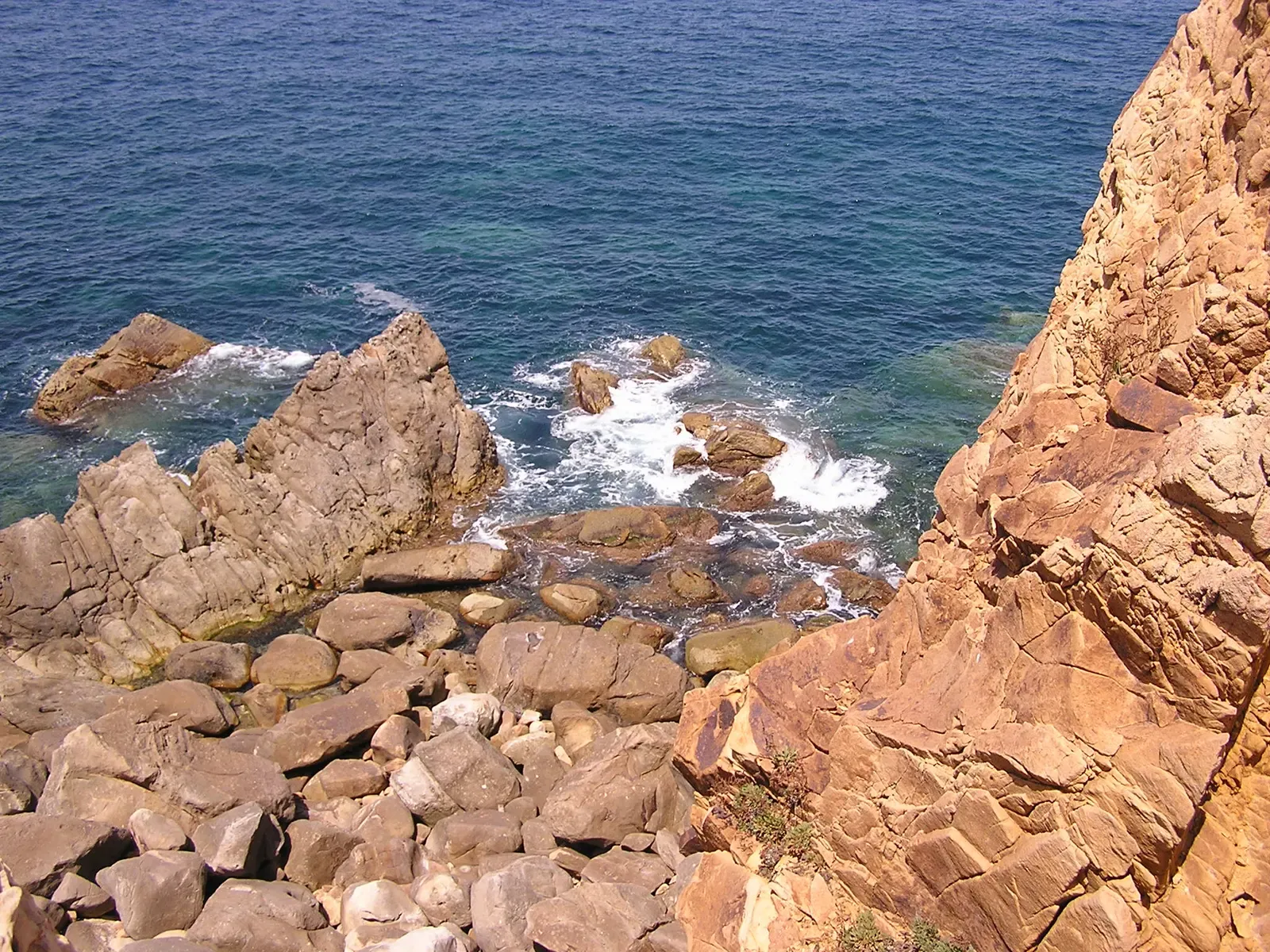 Clear turquoise water surging over ochre rocks below a coastal massif