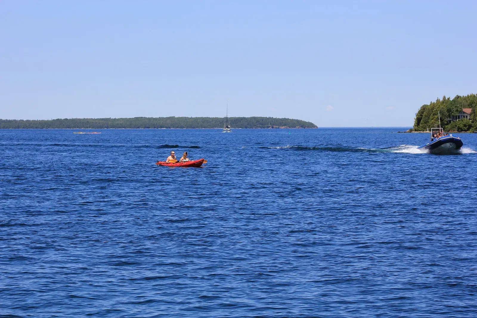 Kayakers and a small boat crossing calm blue water off Tobermory, Ontario