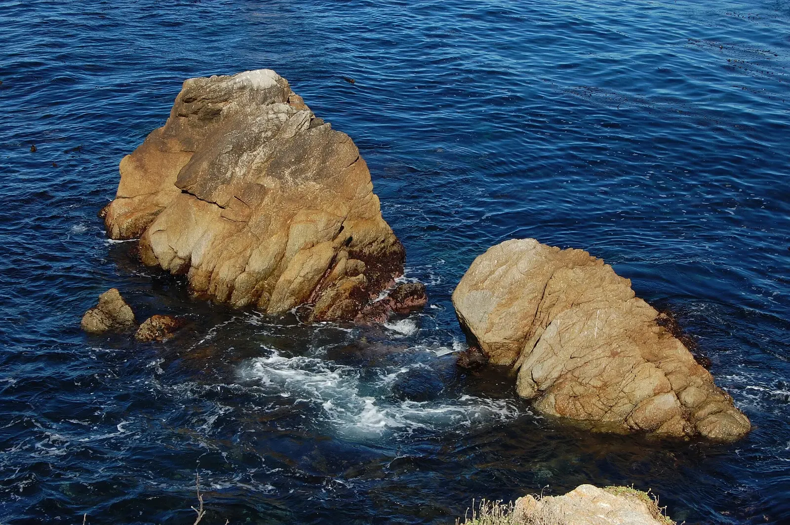 Sunlit granite boulders rise from blue water at Whalers Cove, Point Lobos.