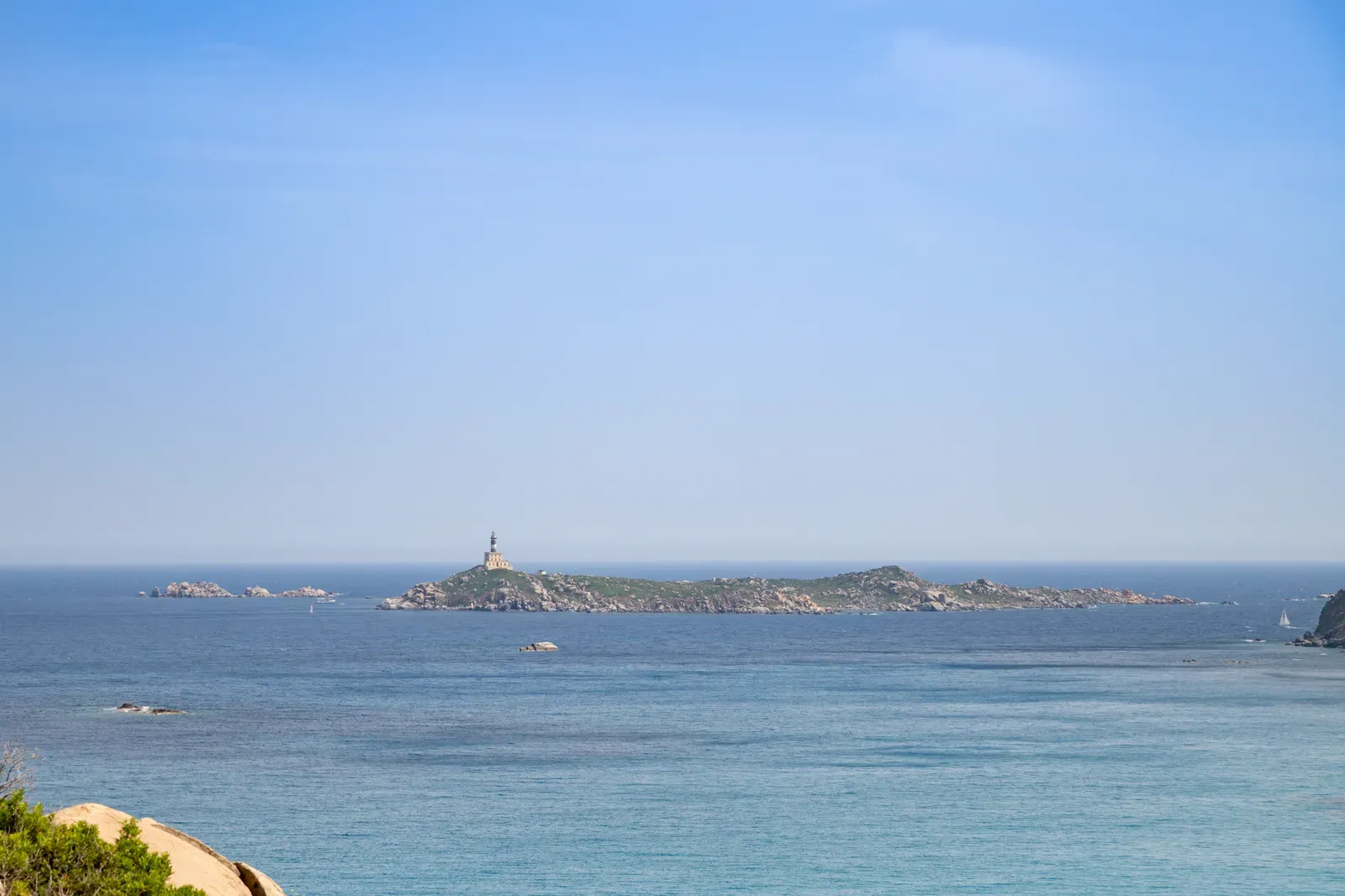 Isola dei Cavoli and its lighthouse seen across calm blue water from the Sardinian shore