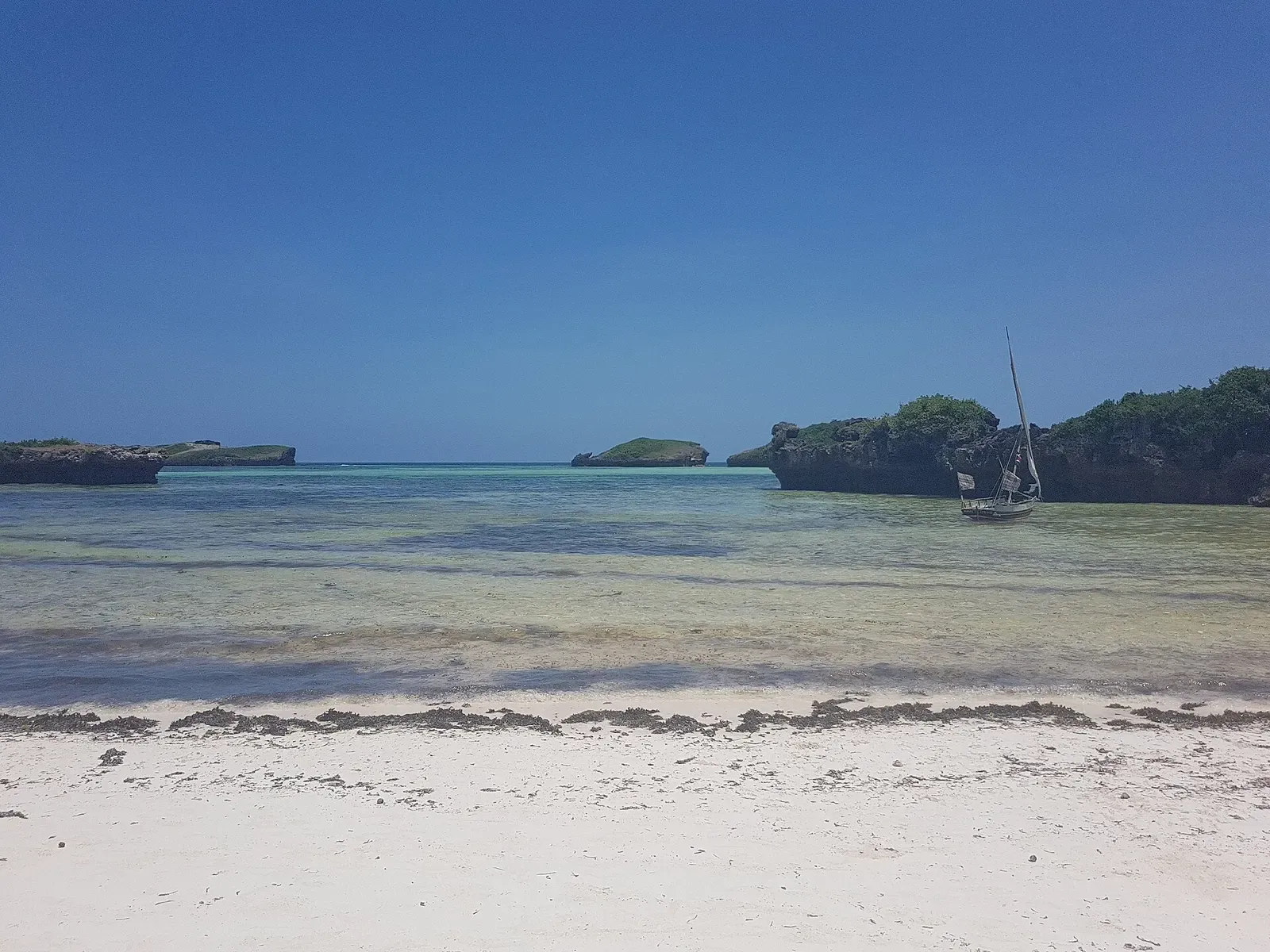 Shallow turquoise lagoon at Watamu with rocky islets and a traditional dhow at anchor