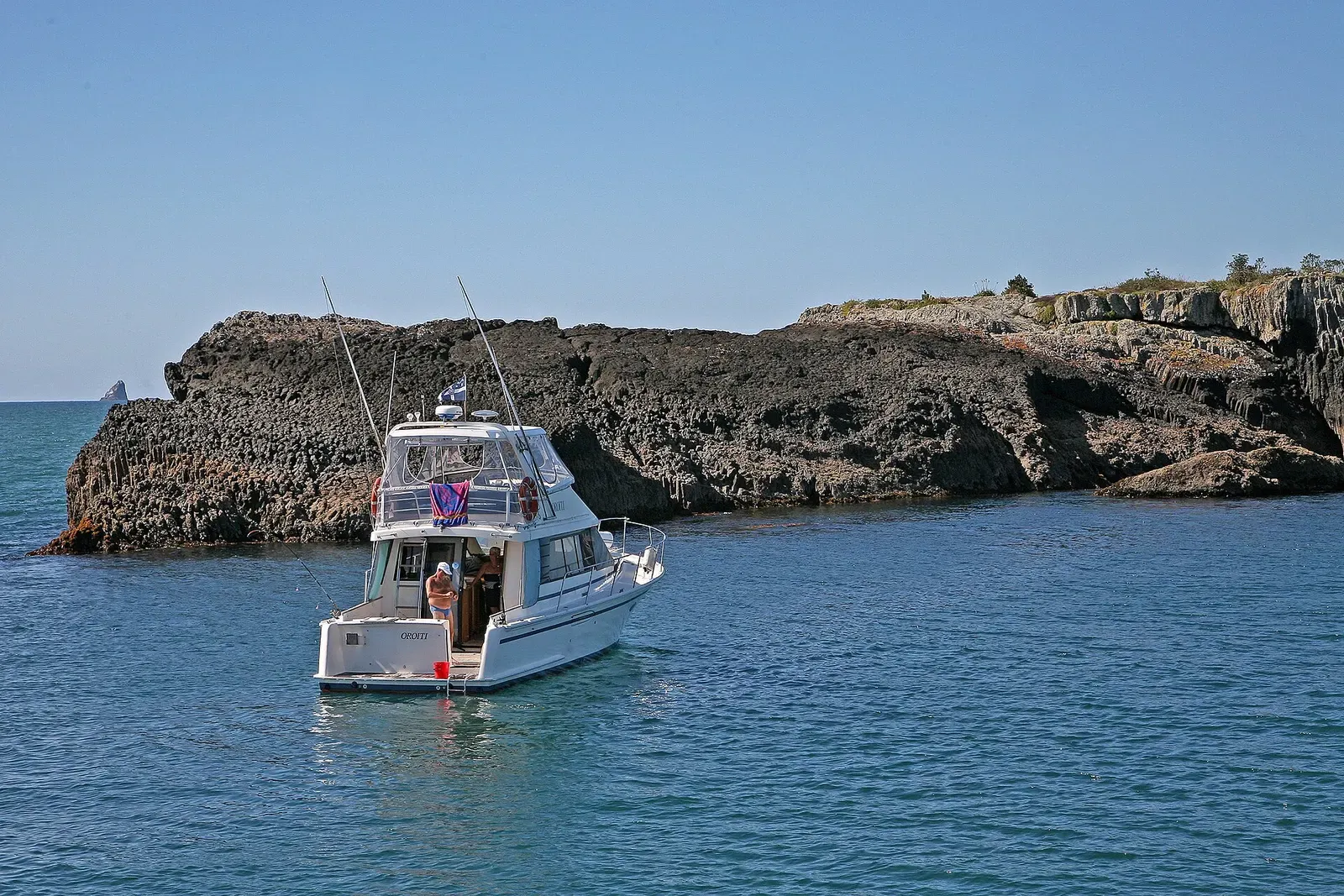 A small boat threads a channel between volcanic rock islets in the Bay of Islands