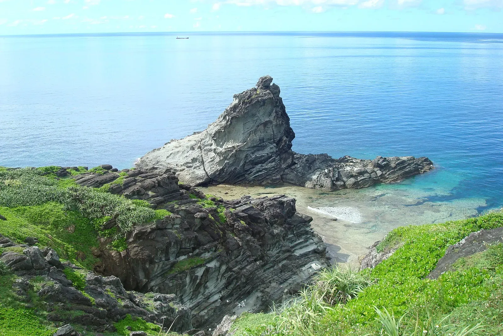 A wind-sculpted sea stack rises from calm blue water at Cape Ugon, Ishigaki.