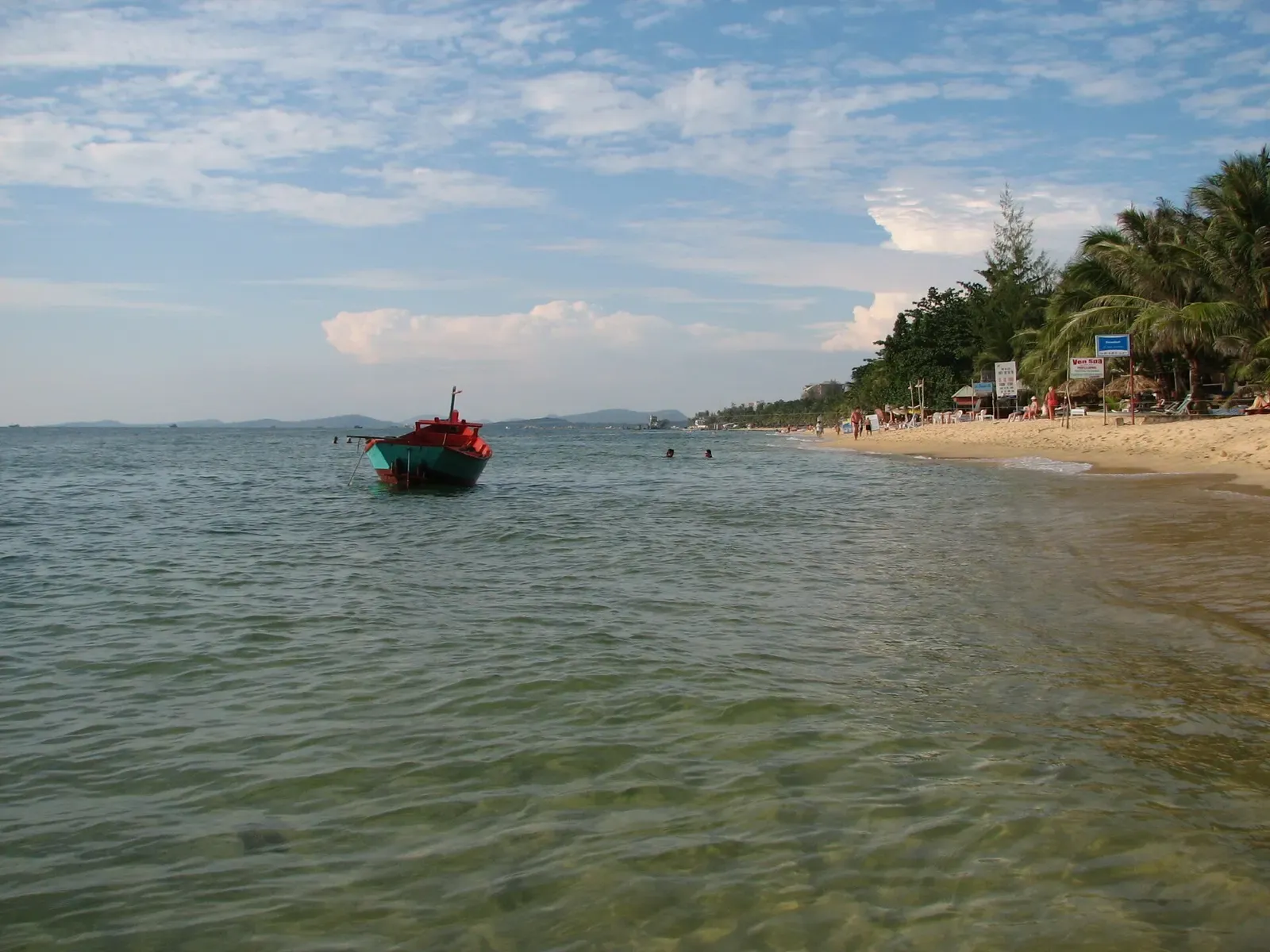 A small fishing boat anchored just offshore along a quiet sandy beach on Phu Quoc