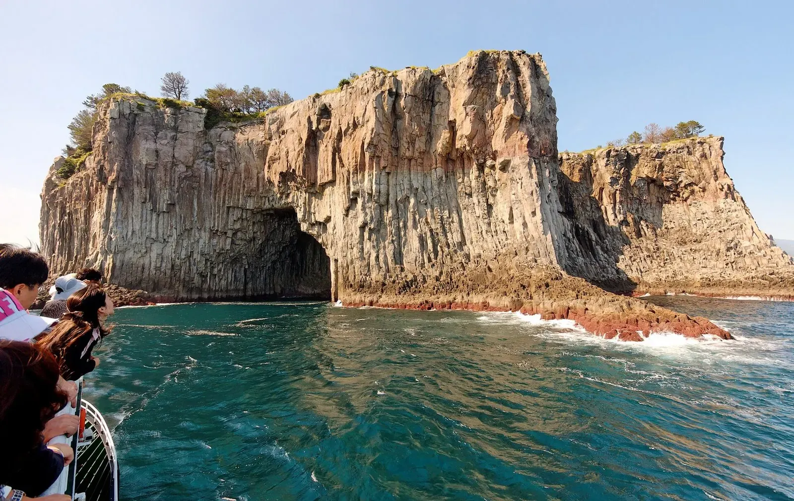 A boat approaches the sheer volcanic cliffs of Beomseom islet near Seogwipo, Jeju.