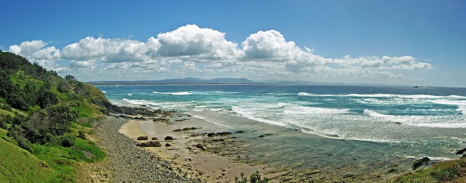 Wide view of Byron Bay's coastline and hills under a cloud-studded sky