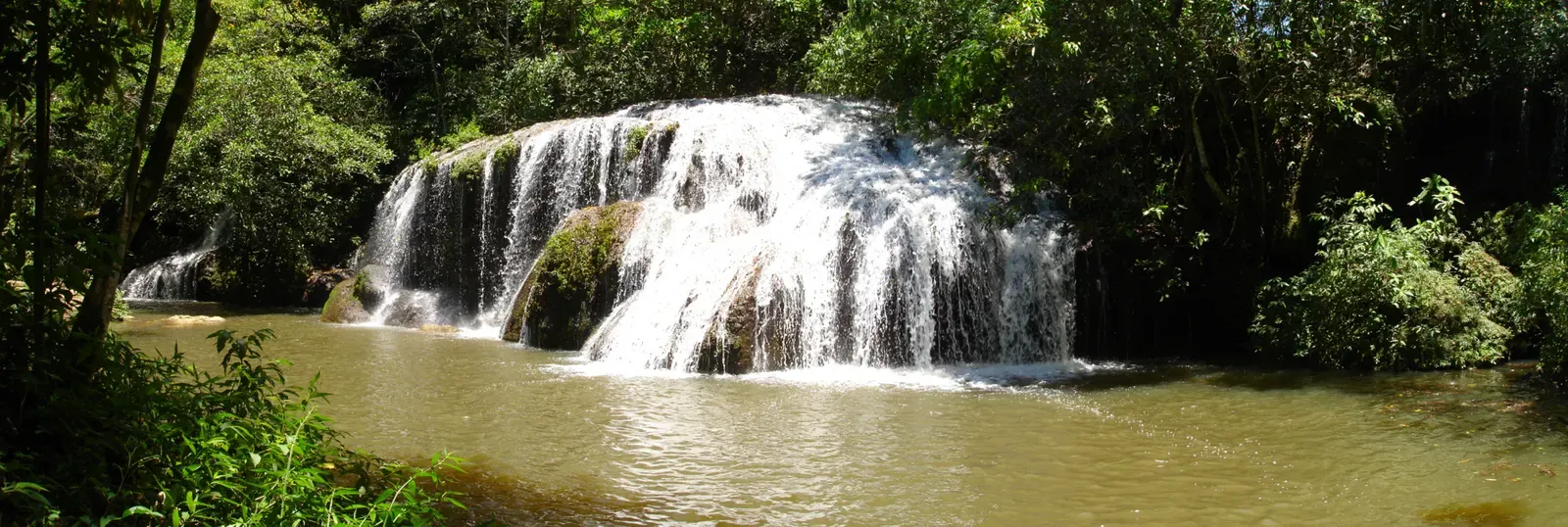 A tiered limestone waterfall cascades into a river pool in the Bonito countryside