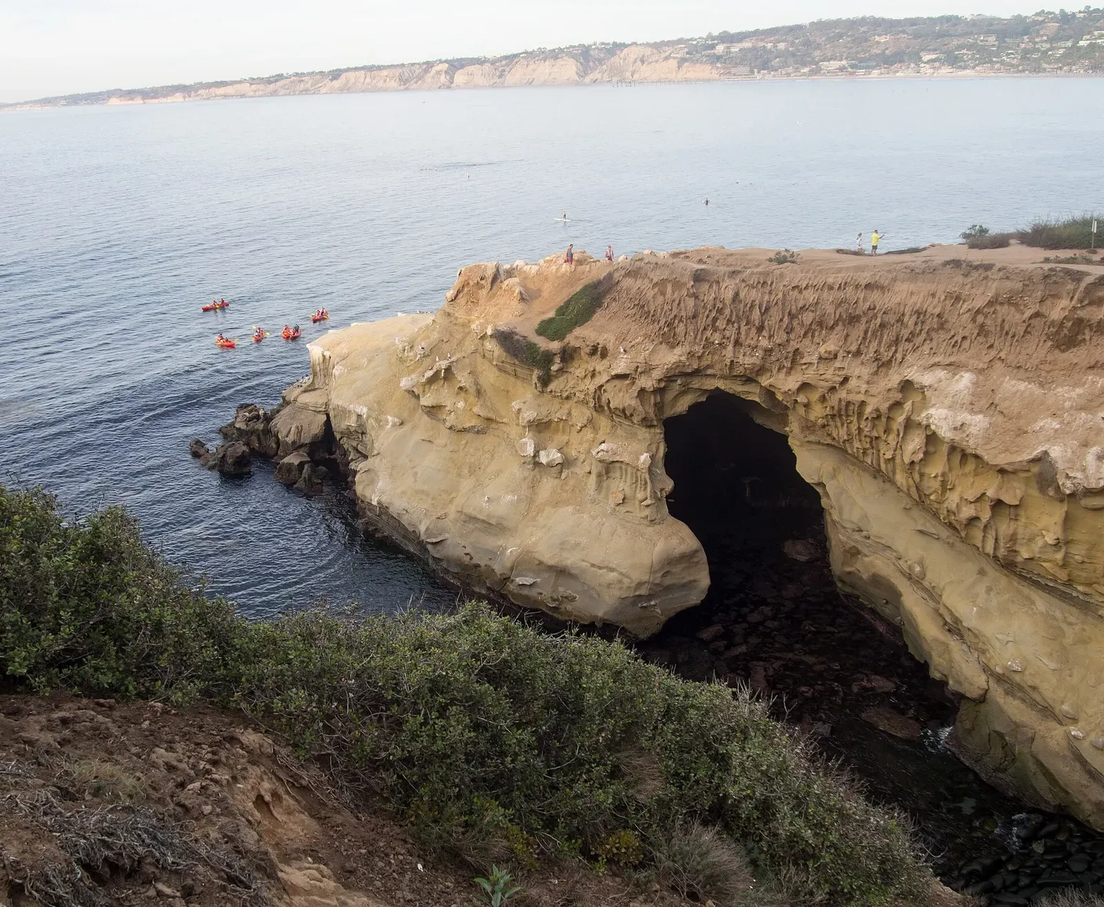 La Jolla Cove shoreline with sea kayakers and swimmers near the sandstone cliffs and arch