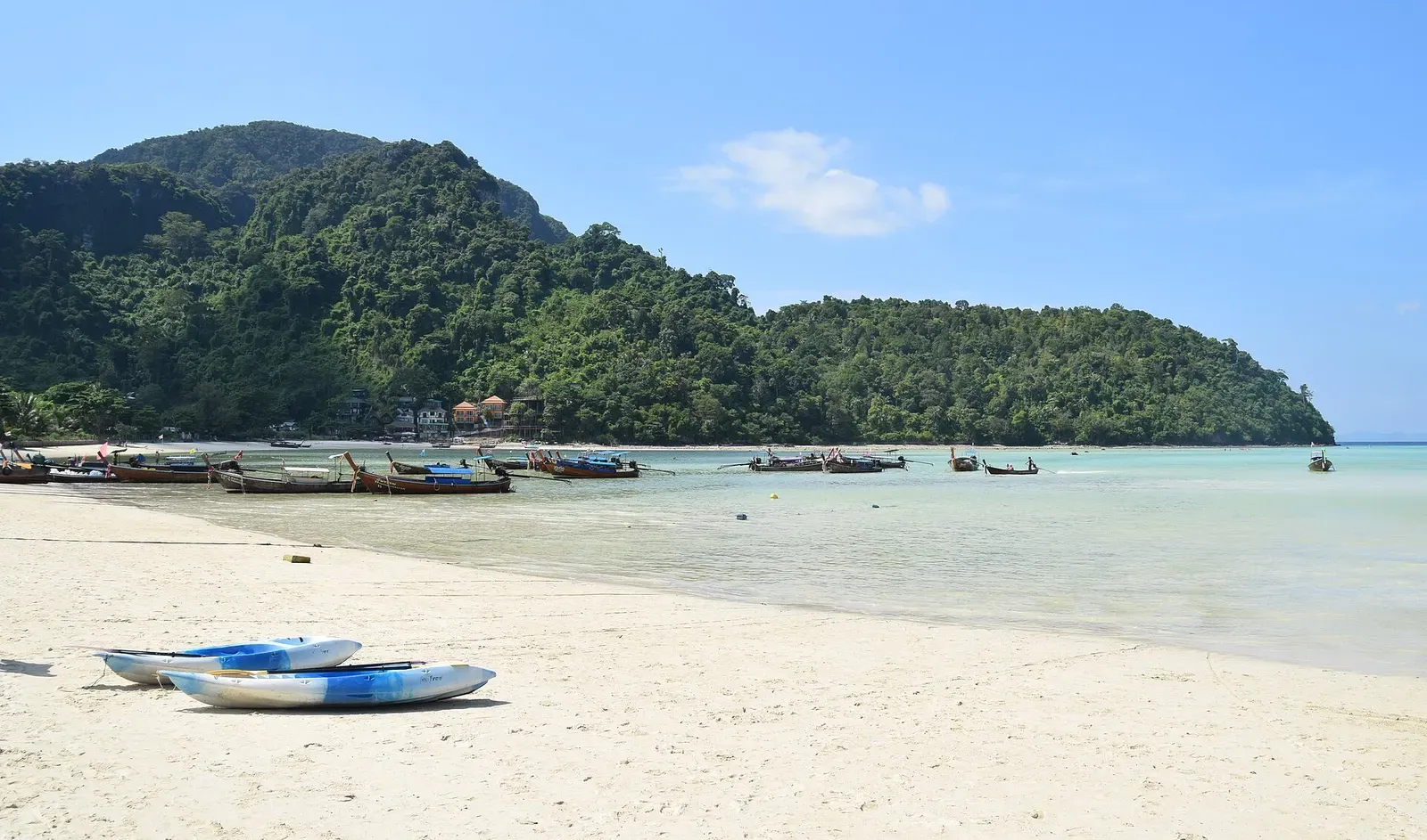 Longtail boats moored off Loh Dalum beach beneath jungle-covered limestone hills