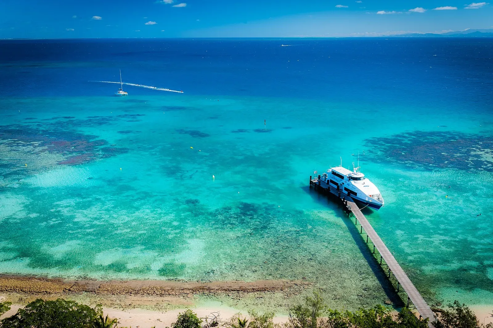 Aerial view of turquoise lagoon water and a dive boat moored at a jetty near Amédée islet