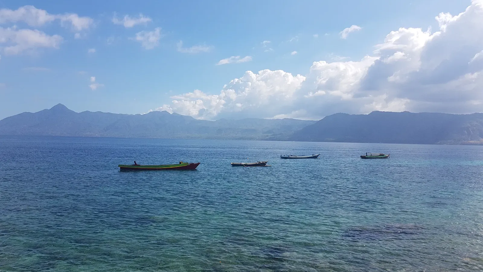 Small fishing boats anchored in calm blue water off Ternate Island with mountains beyond