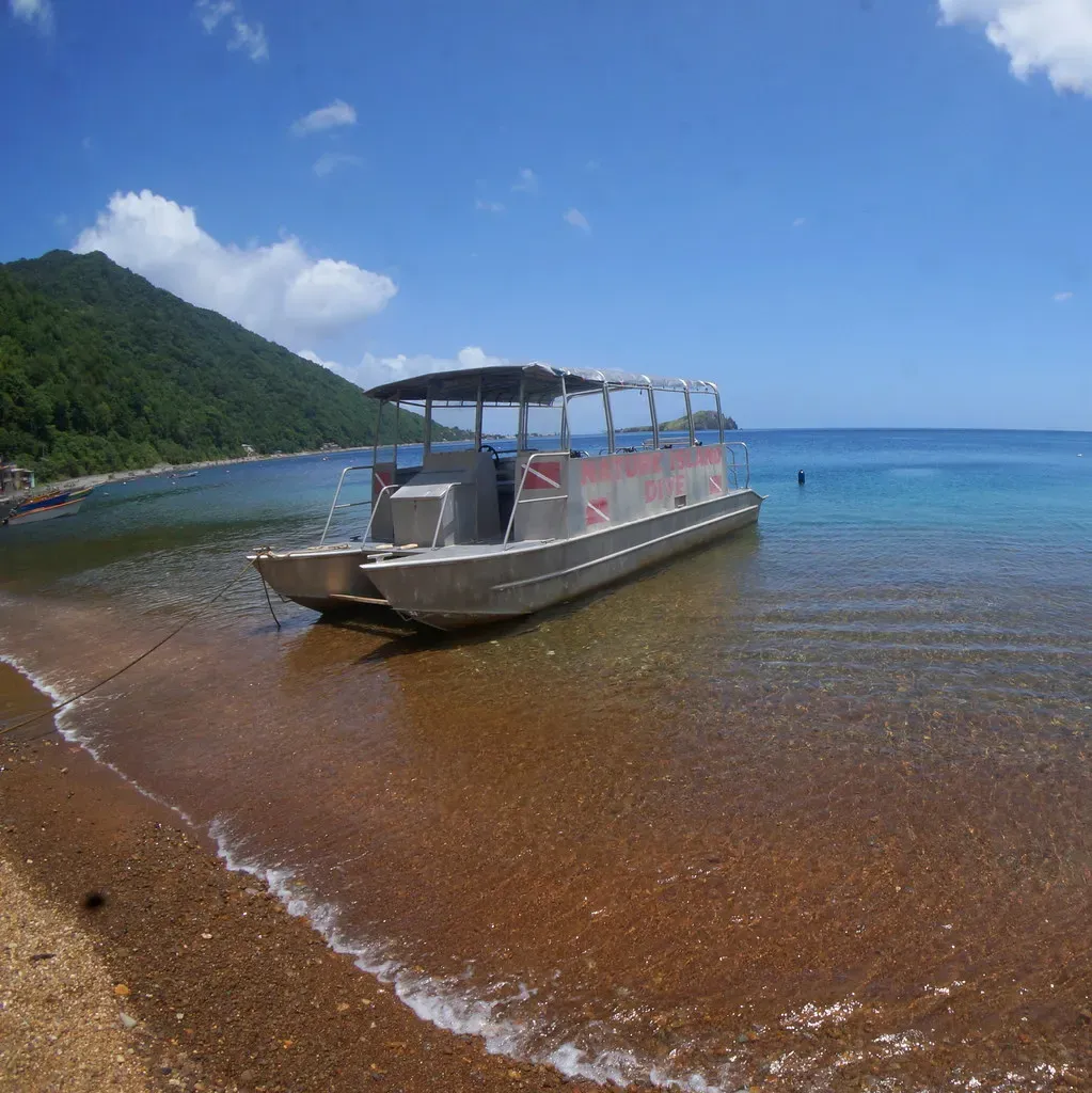 A dive boat idles in the shallows of Soufrière Bay, Dominica, beneath forested hills.