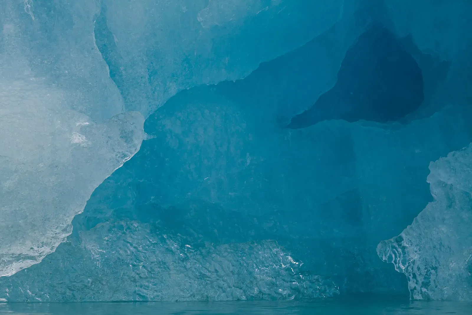 Deep blue light glowing through a hollow in an iceberg near the Svalbard waterline