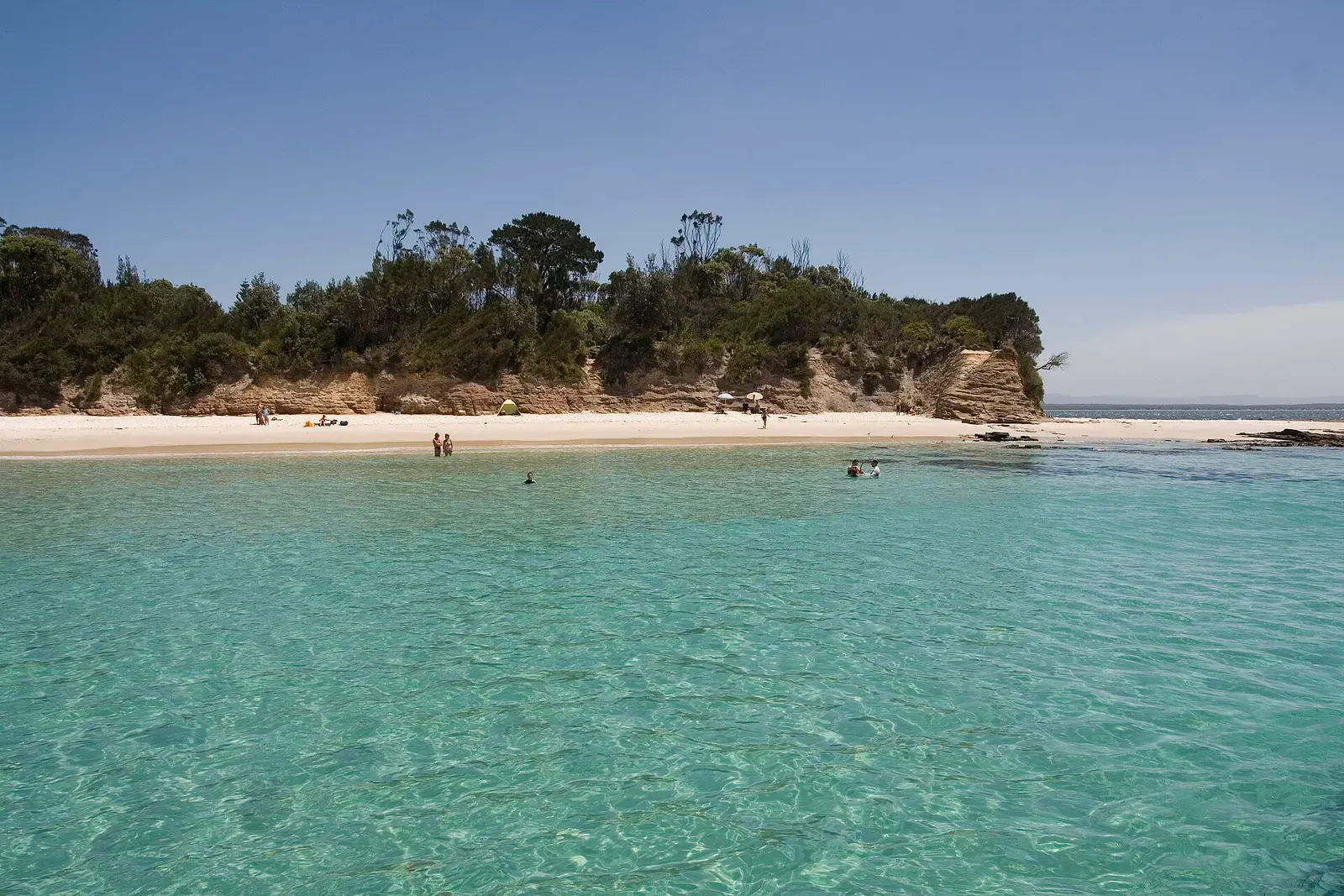 Clear turquoise water meeting a bushy sandstone headland on Jervis Bay