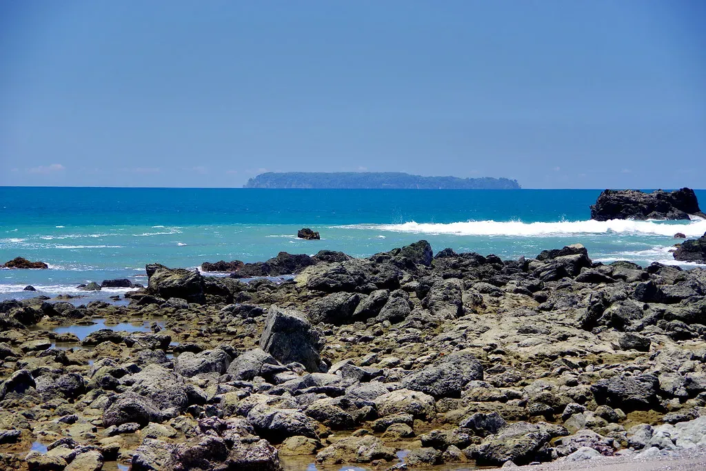Volcanic rocks along the shoreline with Isla del Caño visible offshore across turquoise water