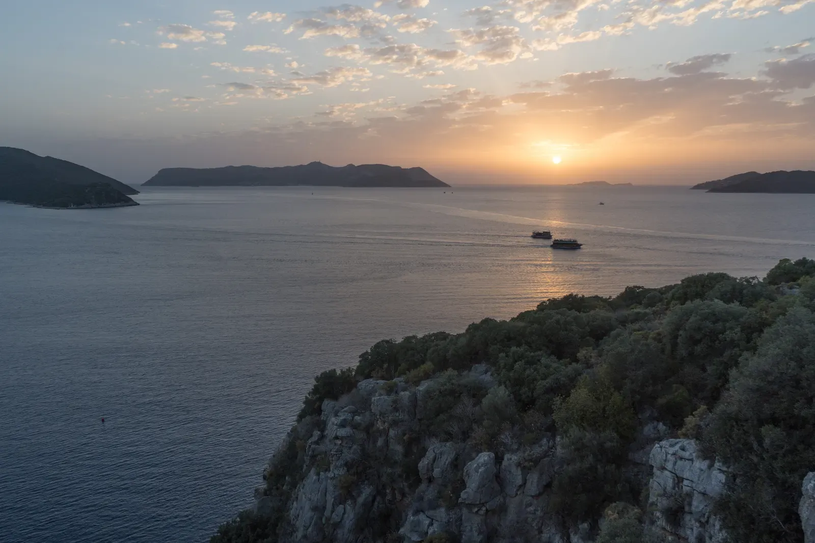 Sunset over the bay of Kaş with boats crossing calm water below dark peninsula silhouettes