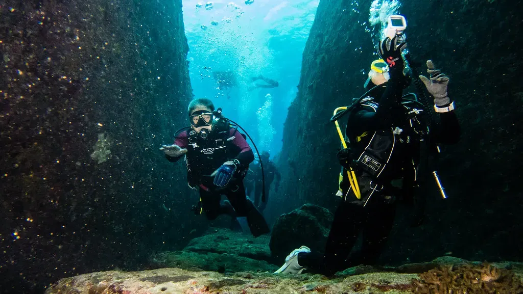 Two divers descend through a narrow rock canyon in Yonaguni's volcanic terrain.