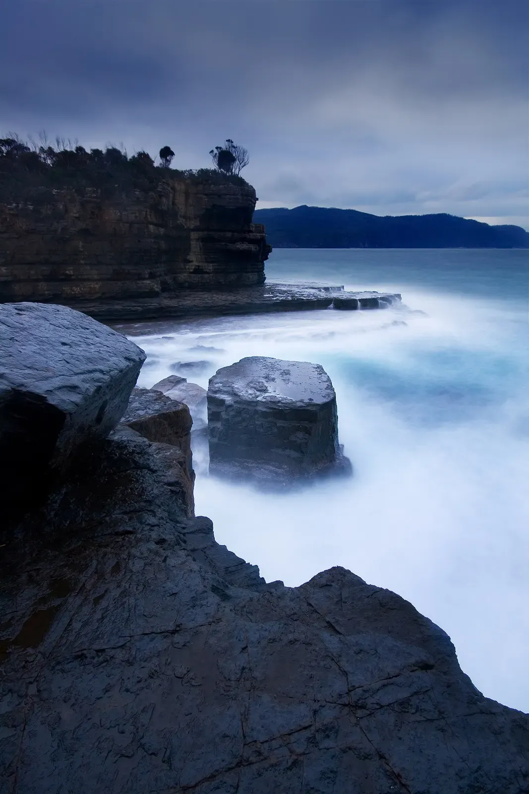 Long-exposure view of mist and sea swirling around rock stacks at Fossil Bay, Tasman Peninsula.