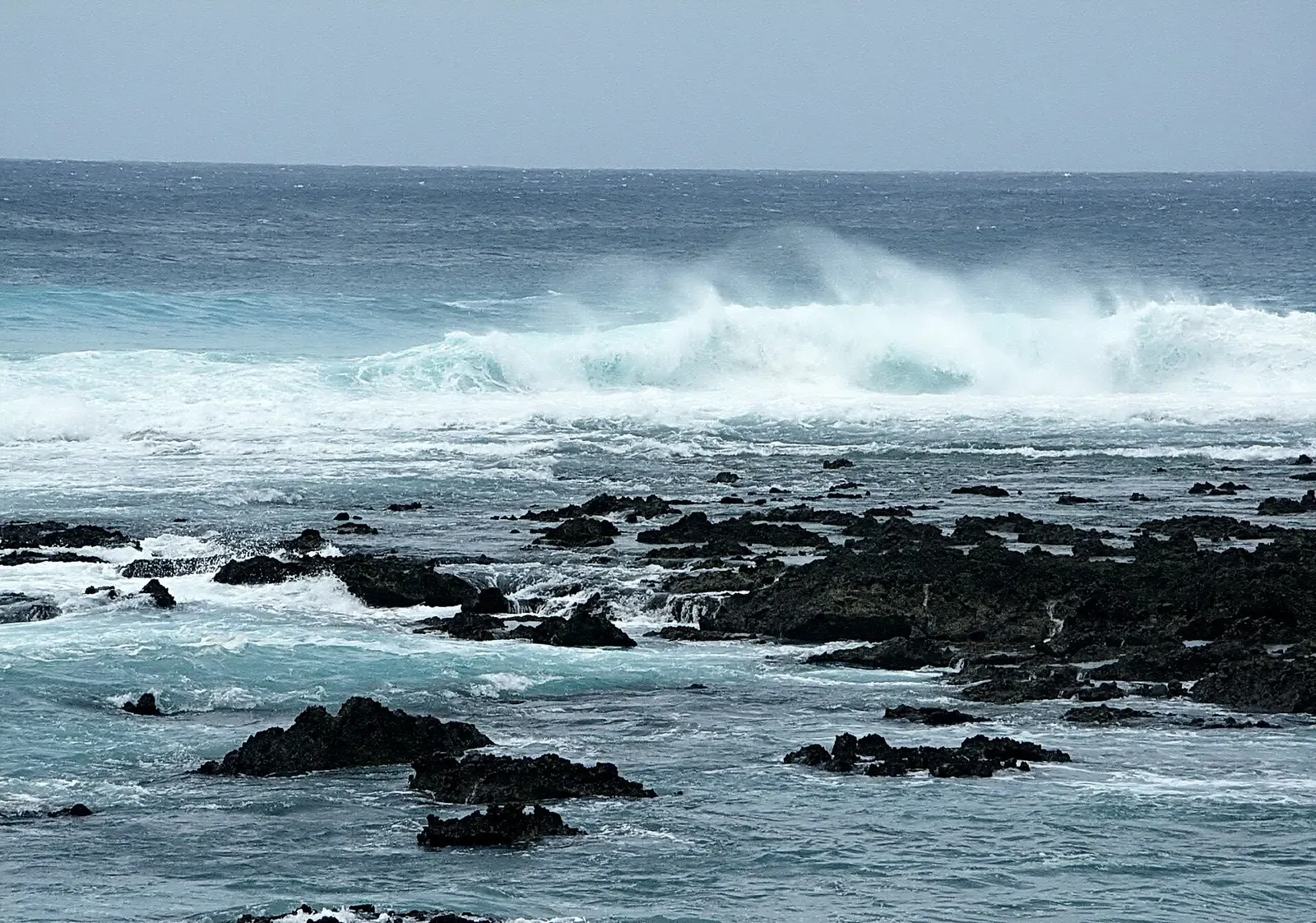 Waves crash over volcanic rocks along Green Island's rugged coast